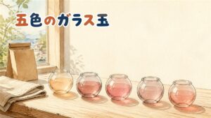午後の窓辺の木のテーブルに並ぶ、丸いガラス玉のような容器5つ。それぞれ中身の色が違い、光が透けて木目に色の影を落としている