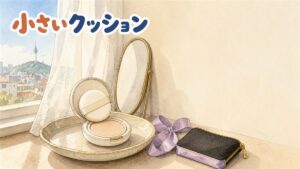 窓辺の化粧台に置かれた丸いミニクッションファンデのケース。開いた蓋にパフが乗り、隣に薄紫のリボンと黒いポーチが並ぶ