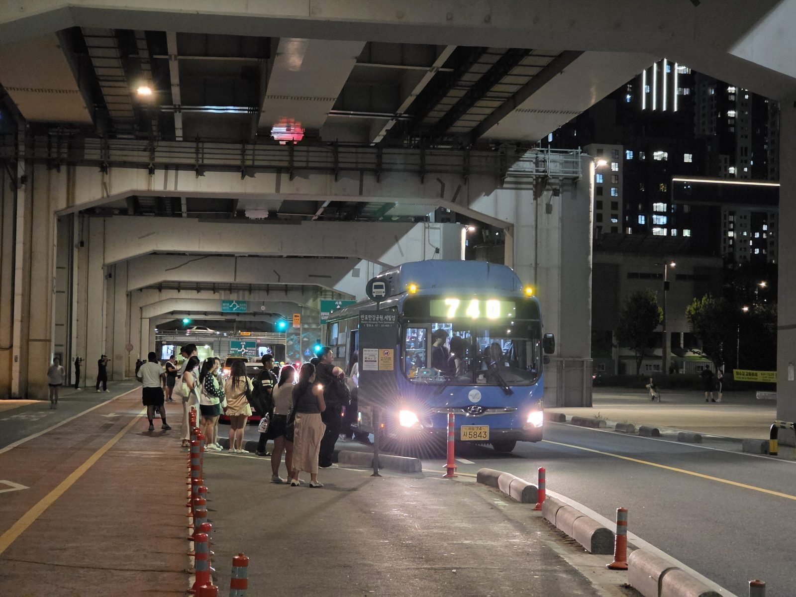 盤浦大橋の下のバス停に止まる青い路線バスと左に並ぶ乗客