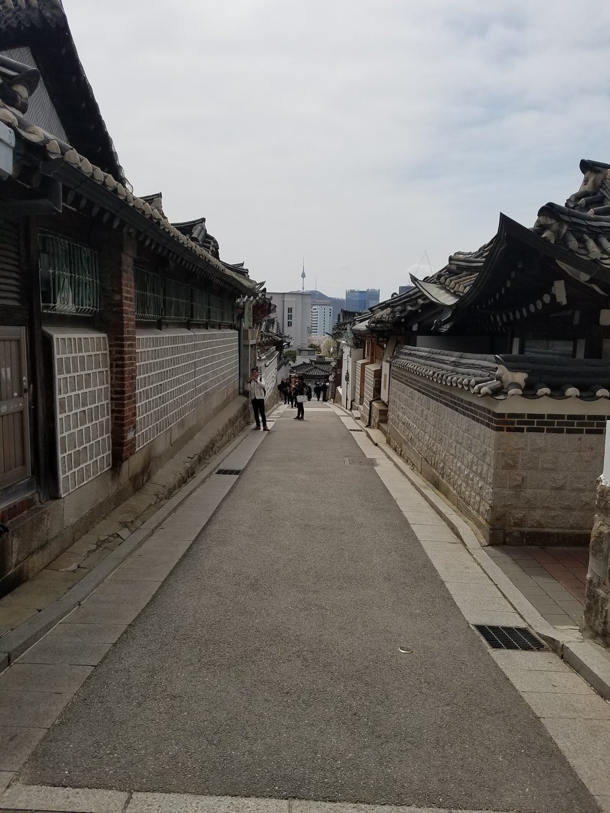 韓屋が並ぶ北村の下り坂の路地と遠くを歩く観光客