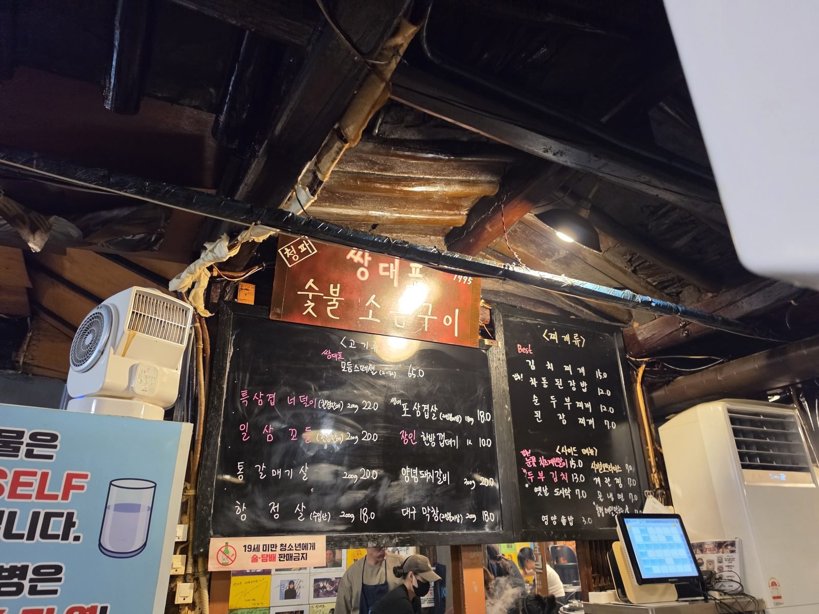 炭火塩焼き店の店内の黒板メニューと木の梁の天井と会計端末