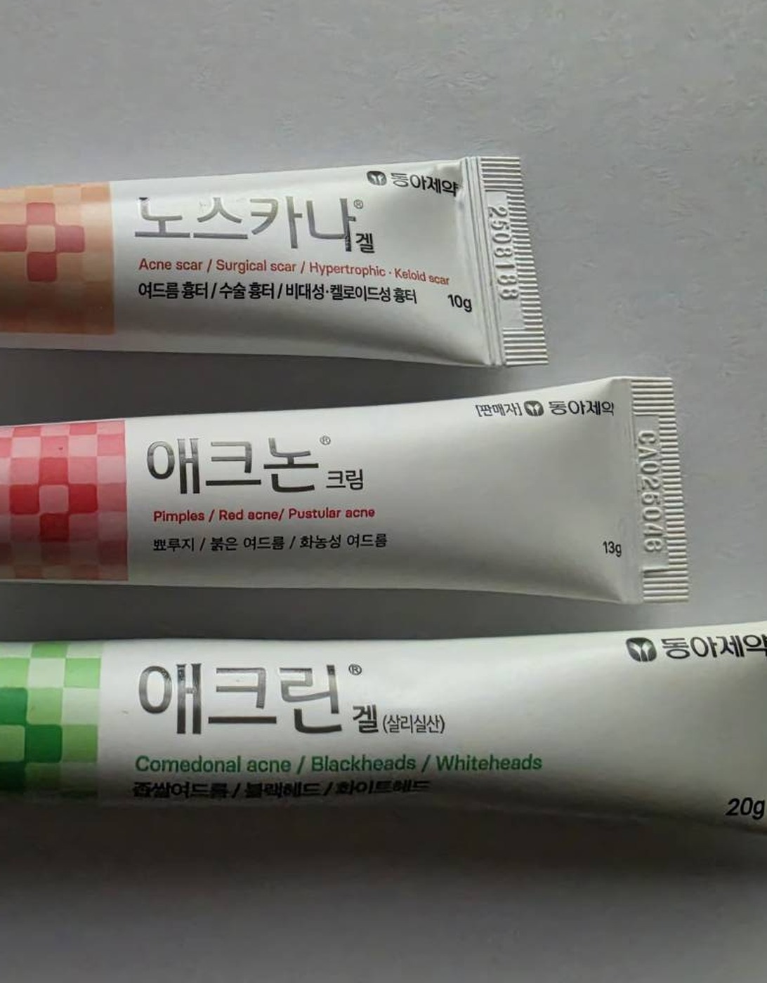 3本のチューブのラベル面を寄って撮った写真。노스카나겔は Acne scar / Surgical scar / Hypertrophic・Keloid scar と10g、애크논크림は Pimples / Red acne / Pustular acne と13gで[판매자]동아제약の表記、애크린겔(살리실산)は Comedonal acne / Blackheads / Whiteheads と20gで동아제약の表記が読める