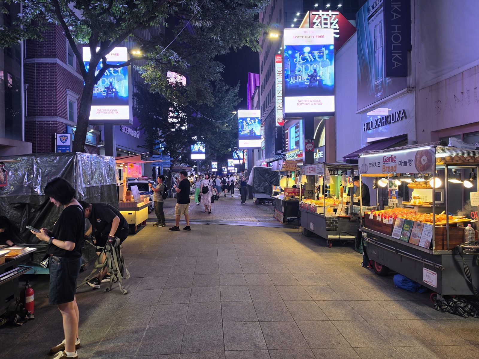 夜のオレンジ色に光る屋台が並ぶ通りとスマホを見る人