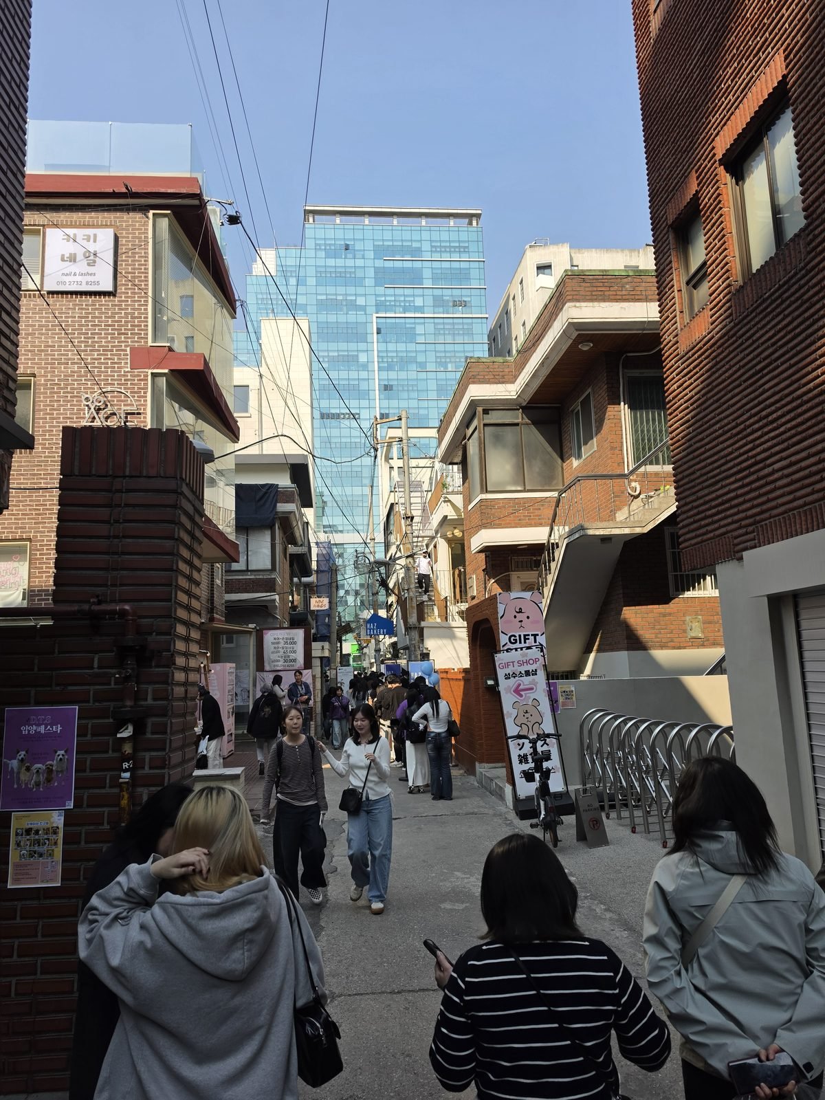 奥にガラス張りの高層ビルが見える細い路地と通行人