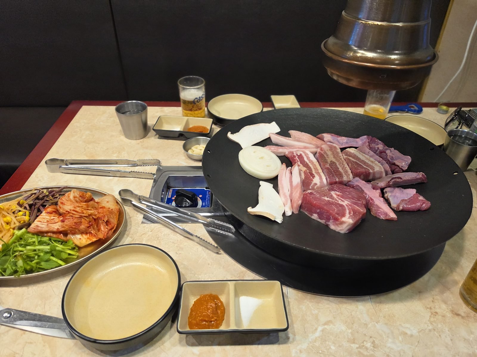 丸い鉄板で焼くサムギョプサルとキムチなどのおかず