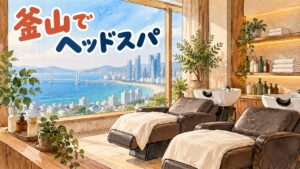 海と高層ビル、長い橋が見える窓辺の美容室を描いた水彩イラスト。シャンプー台つきのリクライニングチェアが2台並び、白いタオルがかけてある。棚にはたたんだタオルとラベルの無いボトル、観葉植物。人物はいない。左上に「釜山でヘッドスパ」の手書き文字
